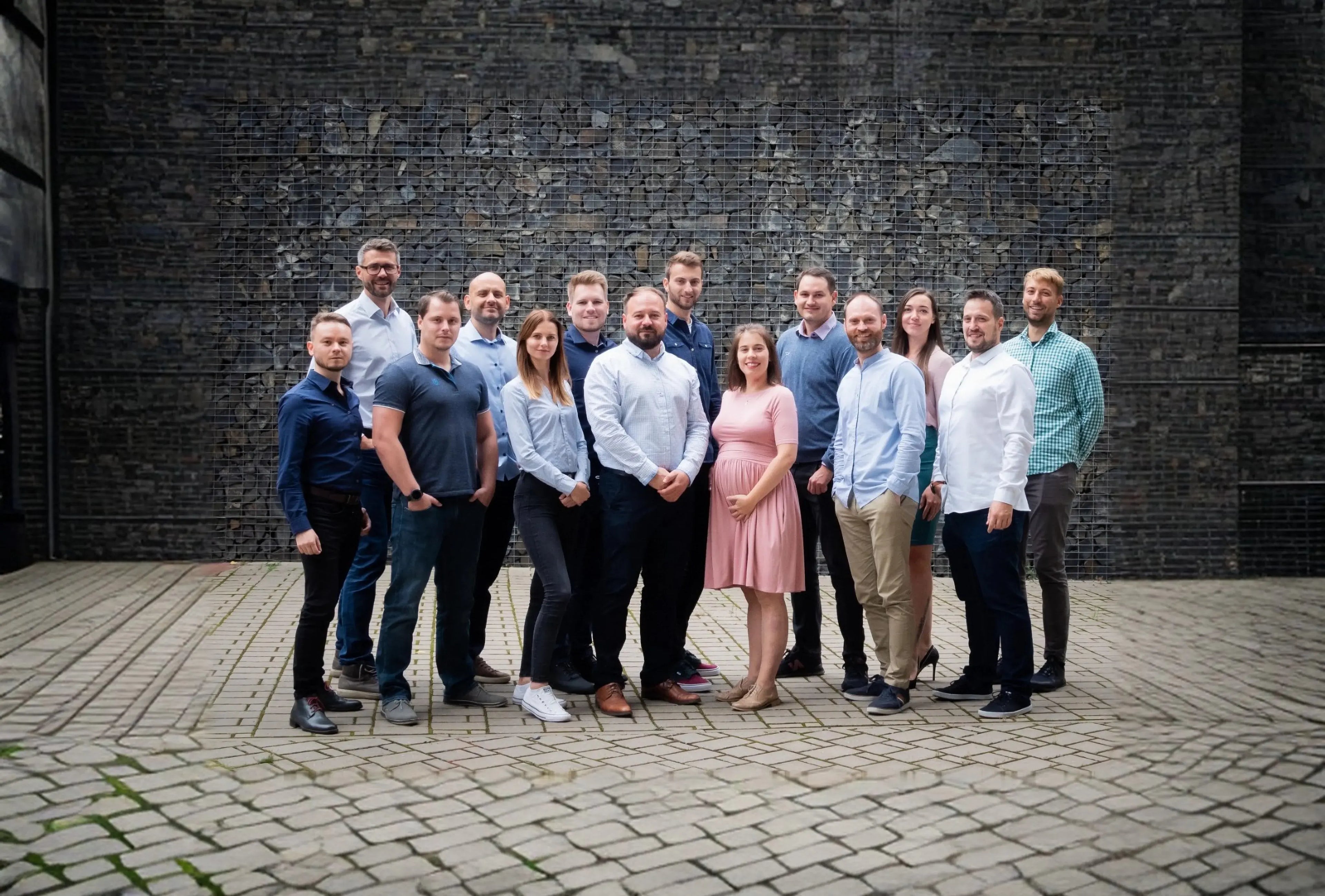 Tým GPS Dozor – skupinová fotografie týmu na venkovním dlážděném nádvoří před kamennou zdí