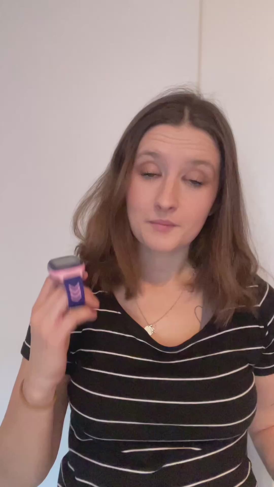 Žena v pruhovaném tričku drží v ruce dětské hodinky KLOKI a vysvětluje, proč si je vybrala pro své dítě. Video má neutrální, světlé pozadí a žena komunikuje přímo směrem ke kameře.